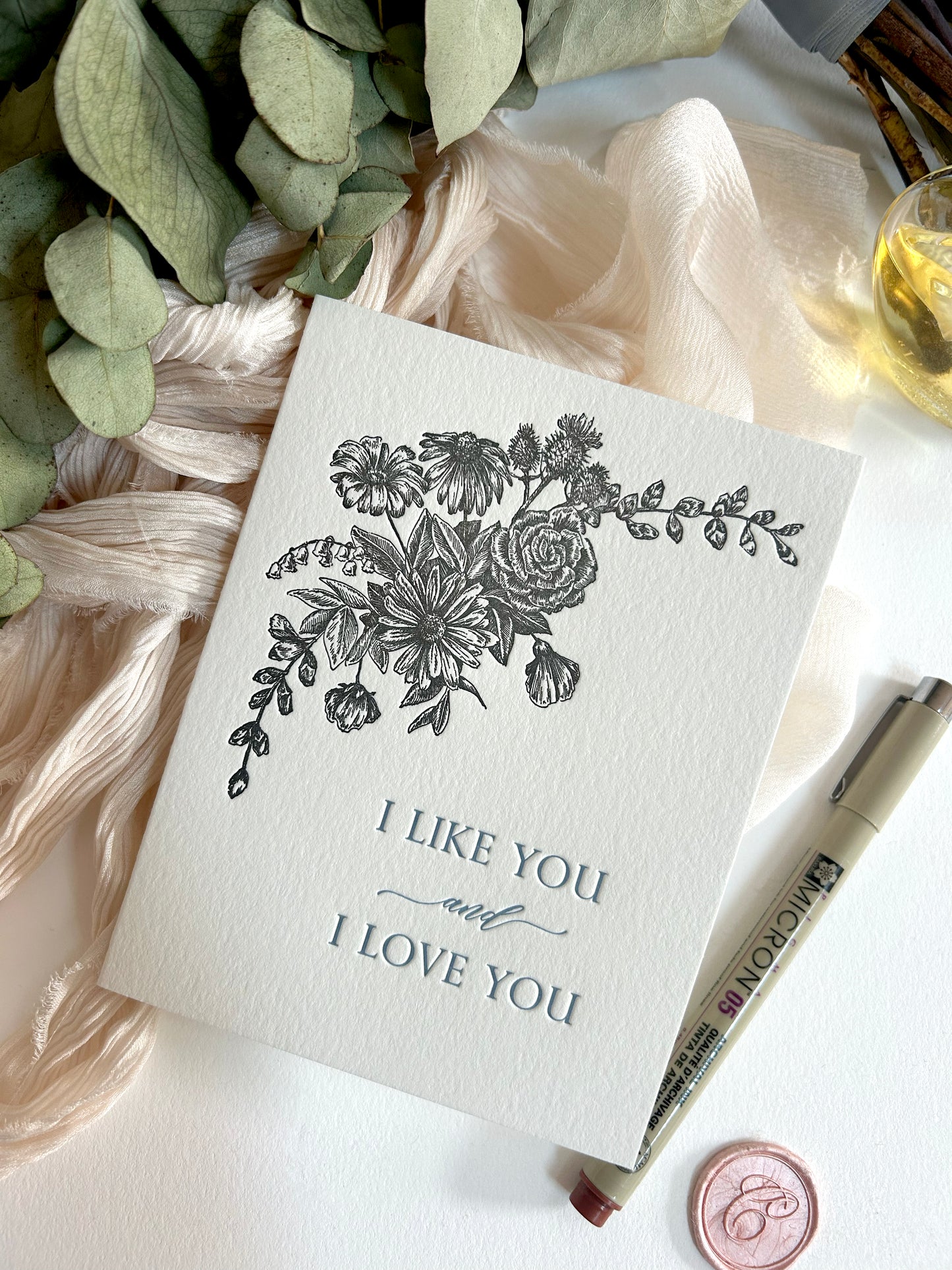 A style shot of Rust Belt Love's love letterpress card with black florals that reads "I like you and I love you"