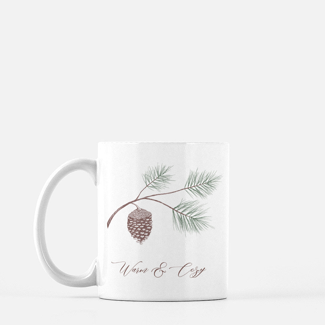White ceramic mug with evergreen and pinecone drawing with the words "Warm & Cozy" by Rust Belt Love