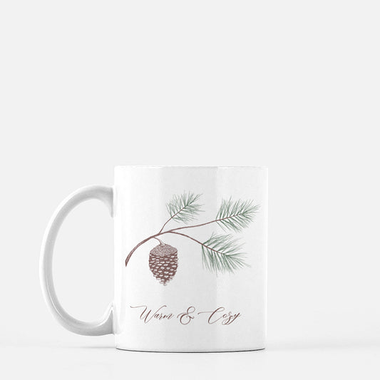 White ceramic mug with evergreen and pinecone drawing with the words Warm & Cozy