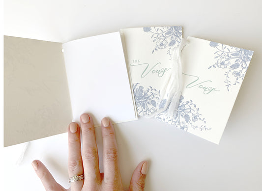 A few letterpress vow books with florals that say " Her Vows" or "His Vows" by Rust Belt Love, one is opened to show a blank inside